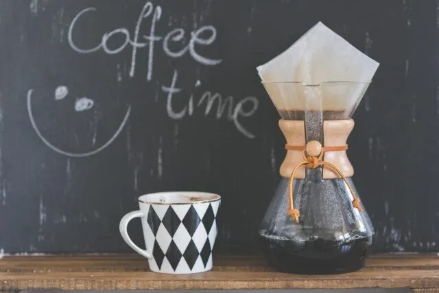 Apă fierbinte turnată peste cafea măcinată într-un filtru, pe o masă de bucătărie
