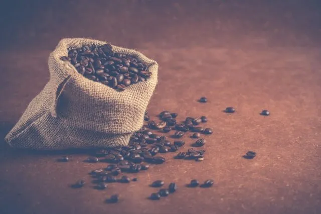 Pungă cu cafea boabe prăjită, așezată pe o masă de lemn